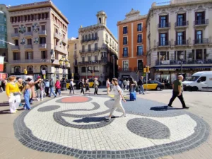 A sunny day in Barcelona, travellers walk across the Joan Miró mosaic on the floor of Las Ramblas Barcelona