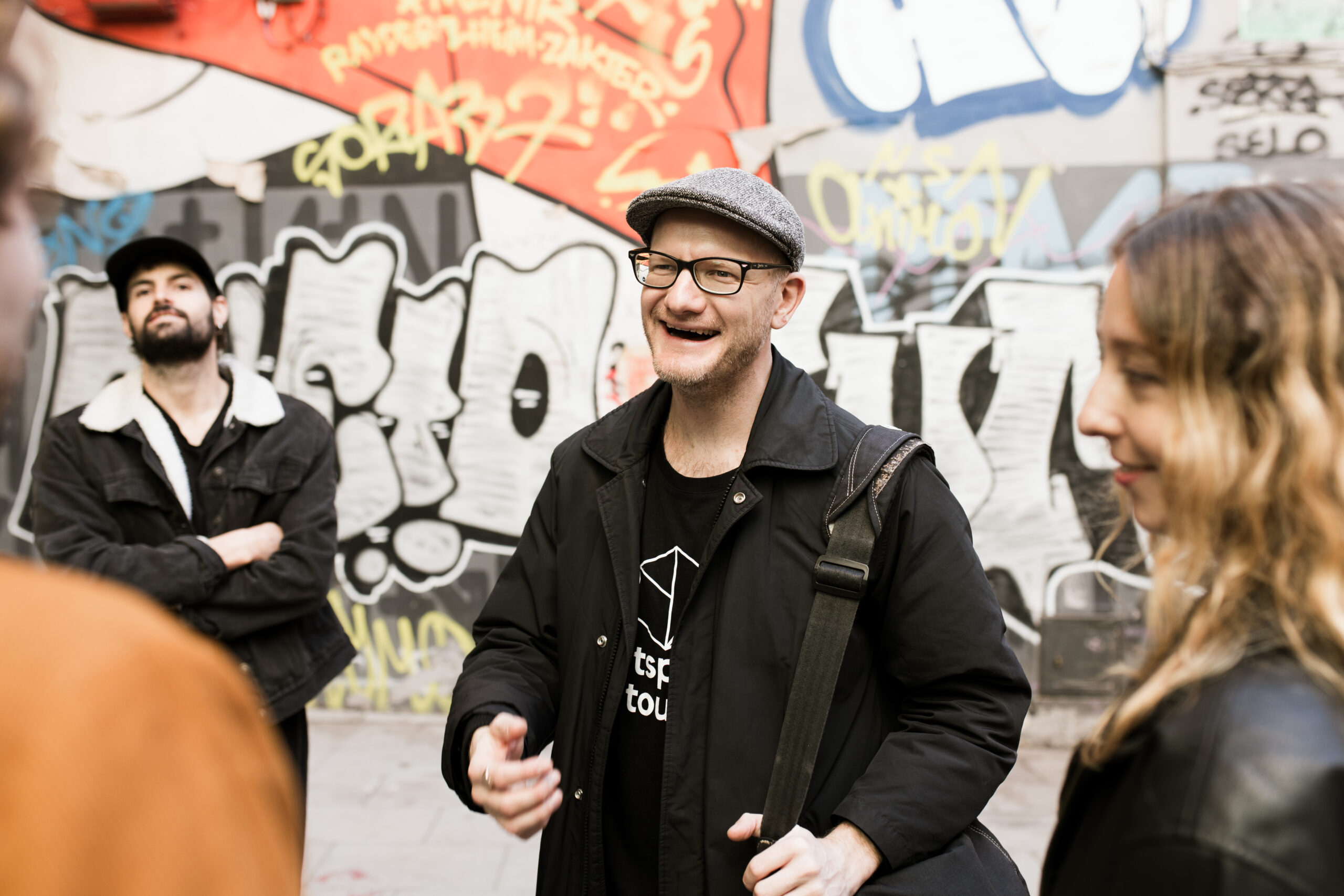 Tour guide laughs with group in front of graffiti on wall