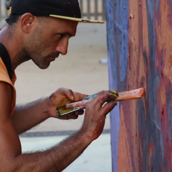 Artist with cap on paints on wall with a brush and look of determined concentration on face